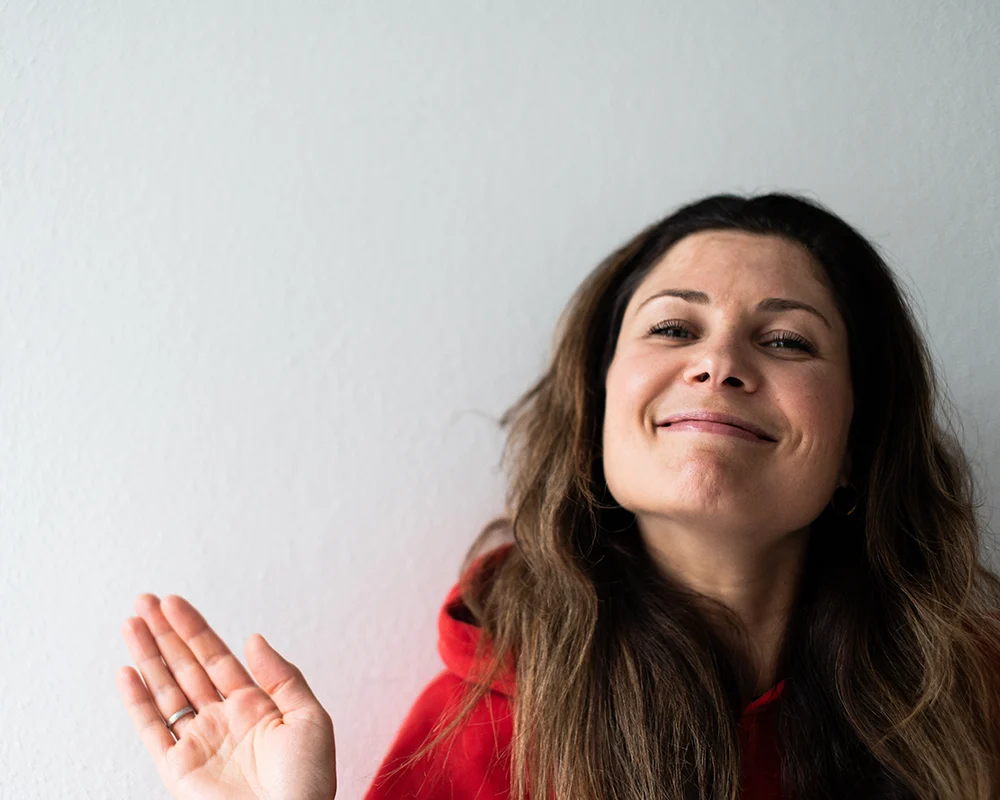 Lena Heinemann Porträtfotografie Stuttgart, Bild einer Frau in einem roten Pullover, die verschmitzt in die Kamera guckt